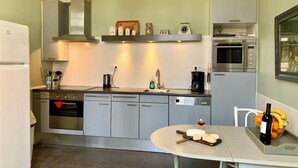 A modern kitchen with stainless steel appliances, a dining table with a wine bottle and fruit, and a window with a view. - Former French railway station with private swimming pool and WIFI (Blond)