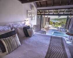 Quarto com cama grande, vista para a piscina e varanda com cadeiras.