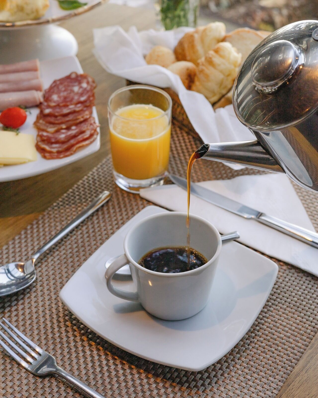 A breakfast setting with a cup of coffee, a glass of orange juice, and a plate of meats and cheese.