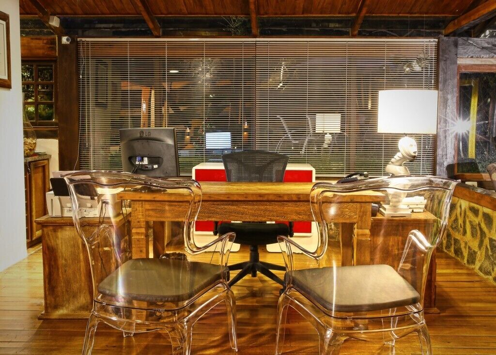 A wooden conference table with four clear plastic chairs, a computer monitor, and a lamp on the table.