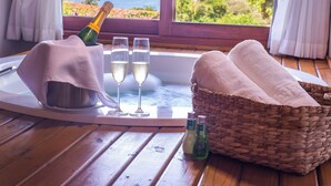 A wooden table with a bottle of champagne, two glasses, a basket of towels, and a view of the ocean through a window. - Pousada Morada dos Bougainvilles (Imbituba)