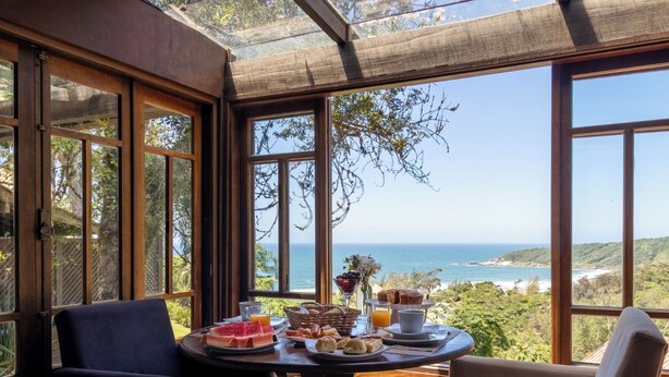 A dining area with a table set for breakfast, overlooking a scenic coastal view. - Pousada Morada dos Bougainvilles (Imbituba)