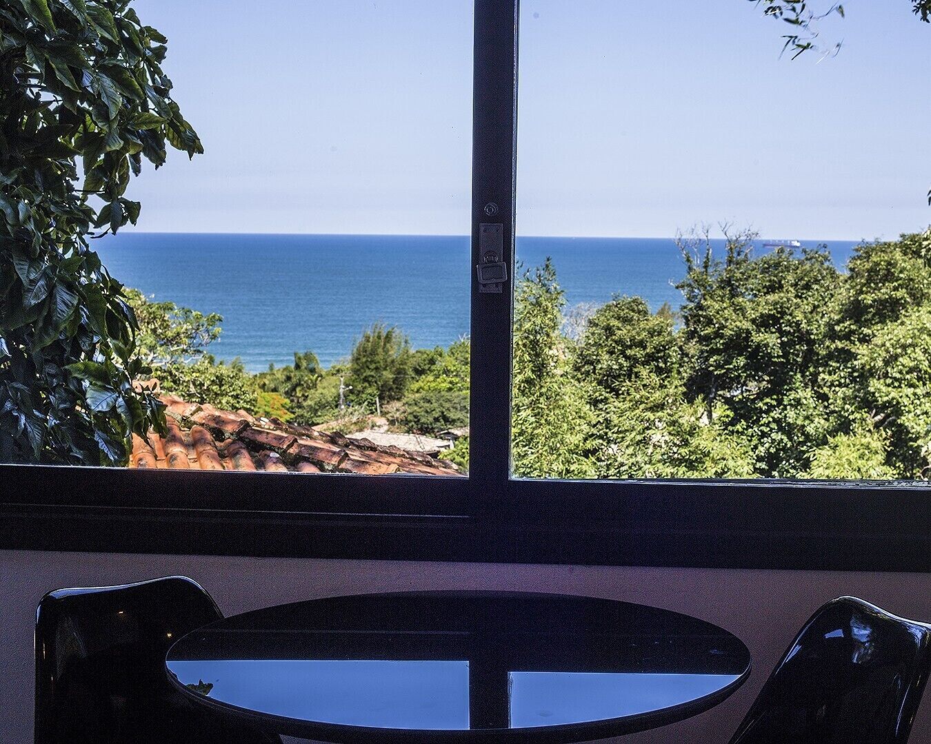 A room with a large window overlooking a coastal view, a round table, and two chairs.