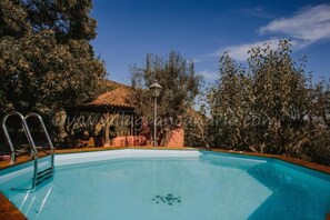 Una piscina con escalera metálica, rodeada de árboles y un pabellón.