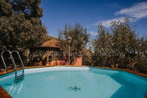 Una piscina con escalera metálica, rodeada de árboles y un pabellón.
