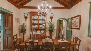 Una sala da pranzo con un tavolo di legno, sedie, un lampadario e una mensola con stoviglie.