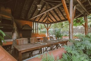 An outdoor dining area with a wooden table set for four, surrounded by chairs, under a thatched roof structure. - Cloty Holiday Rental by VillaGranCanaria (Vega de San Mateo)