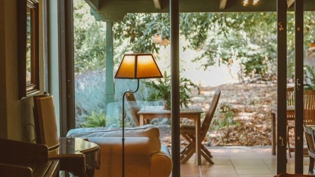 Una stanza con un divano, una lampada e vista su un patio esterno con tavolo e sedie.