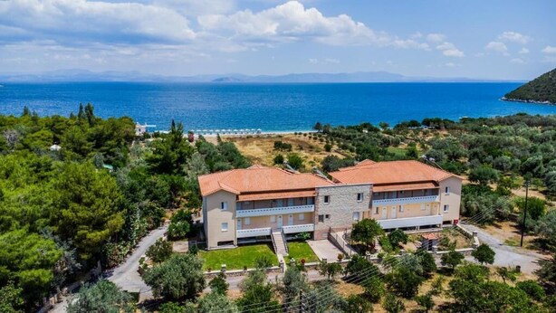 Un edificio de dos pisos con techo de tejas rojas, rodeado de vegetación y vistas al mar.