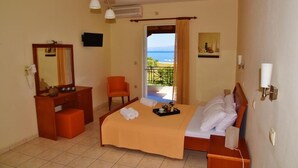 Habitación de hotel con cama, escritorio, silla, espejo de baño y vista al mar desde la puerta del balcón.