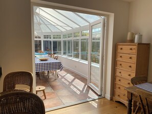 A conservatory with a table and chairs, a wooden dresser, and a view of the outside. - Stylish and Contemporary Home in Chichester within walking distance of Goodwood (Chichester)