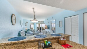A kitchen with granite countertops, a double sink, and a dining area with a table and chairs. - Shore Thing Premium Ocean View Two Bedroom Condo (Treasure Island)