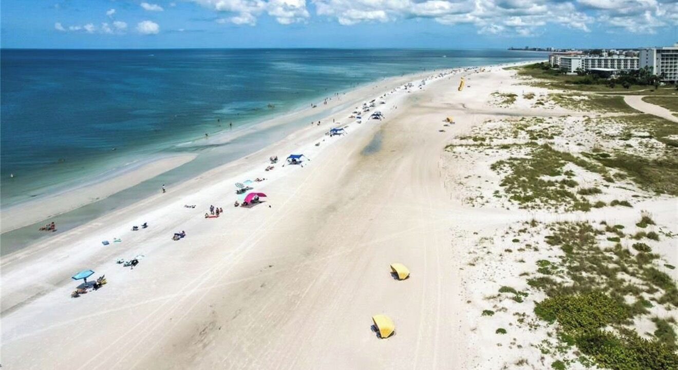A beach with a long stretch of sand, a few umbrellas, and a building in the background.