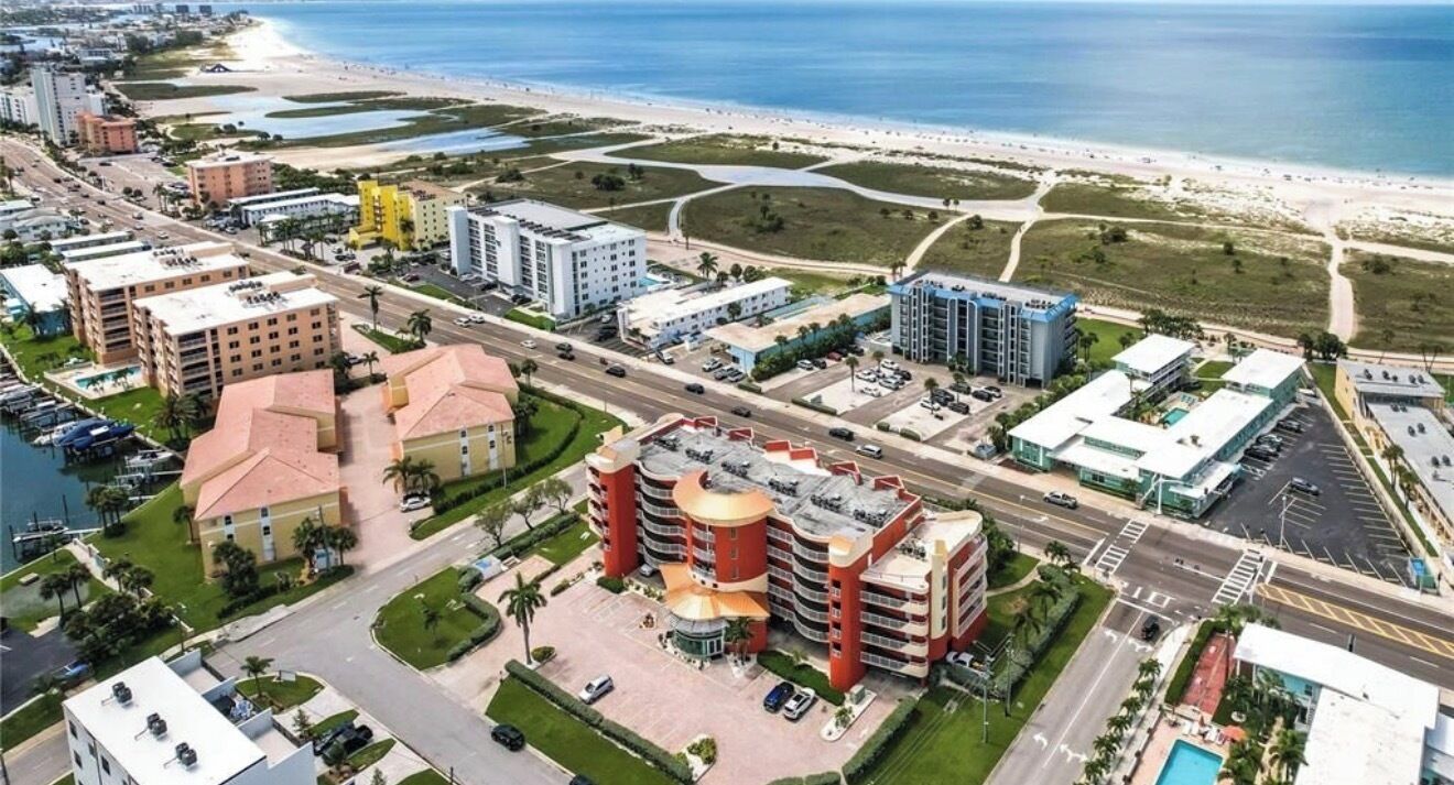 An aerial view of a coastal urban area with a hotel featuring a central courtyard, multiple buildings, and a beach in the background.