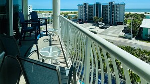 A balcony with a pool, chairs, and tables, overlooking a beach and buildings. - Shore Thing Premium Ocean View Two Bedroom Condo (Treasure Island)