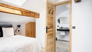A bedroom with a bed, wooden ceiling, a bathroom with a sink and mirror, and a door with a handle. - Montaska - Chalet La Plagne - 7 Suites - Jacuzzi / Sauna (La Plagne Tarentaise)