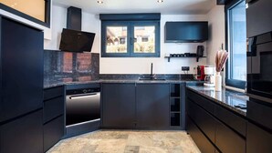 A modern kitchen with dark cabinetry, a built-in oven, and a window overlooking a garden. - Montaska - Chalet La Plagne - 7 Suites - Jacuzzi / Sauna (La Plagne Tarentaise)
