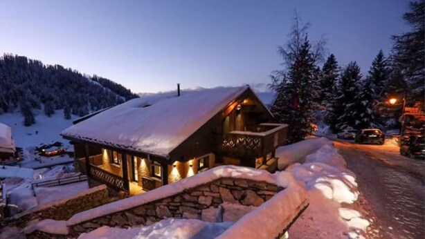 A cozy lodge with a stone facade and a snow-covered roof, surrounded by a snowy landscape and a mountain in the background. - Montaska - Chalet La Plagne - 7 Suites - Jacuzzi / Sauna (La Plagne Tarentaise)