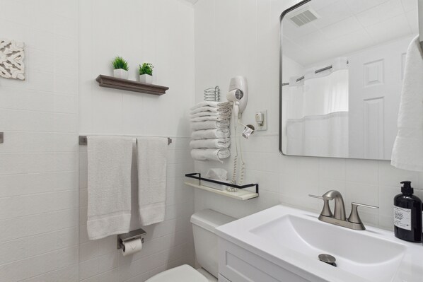 A bathroom with a white sink, a mirror, a towel rack, a toilet, and a hairdryer.