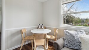 A corner room with a round table and four chairs, a window with a view, and a grey sofa with a fluffy pillow. - Cabin 9 / Pleasant Valley Resort / Hot Tub / Sauna / BBQ (Arcadia)