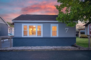 A single-story house with a dark blue exterior, a number '7' on the side, and a visible window with a light inside.