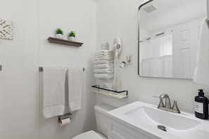Un baño con lavamanos blanco, espejo, toallero, inodoro y secador de pelo.