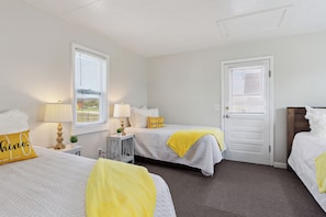 A hotel room with two beds, a door, and a window with blinds.