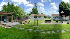 Un patio trasero con un pérgola de madera, una casita y una mesa de picnic.