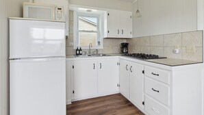 Une cuisine avec des meubles blancs, un réfrigérateur, un four à micro-ondes, un évier et une cuisinière.