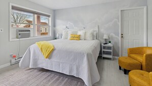 A bedroom with a large bed, a window with blinds, a white door, and a yellow armchair. - The Luxe King Room 5 / Pleasant Valley Arcadia Resort (Arcadia)