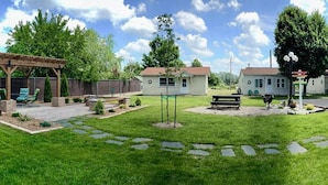Un patio trasero con un pérgola de madera, una casita y una mesa de picnic.