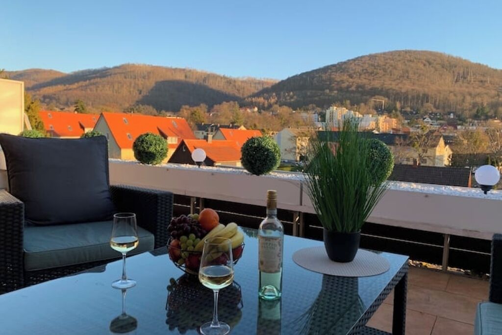 A terrace with a table set for two, featuring a bottle of white wine, a bowl of fruit, and a potted plant.