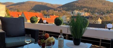 Eine Terrasse mit Tisch für Zwei, mit einer Weinflasche, Obstschale und einem Blumentopf.