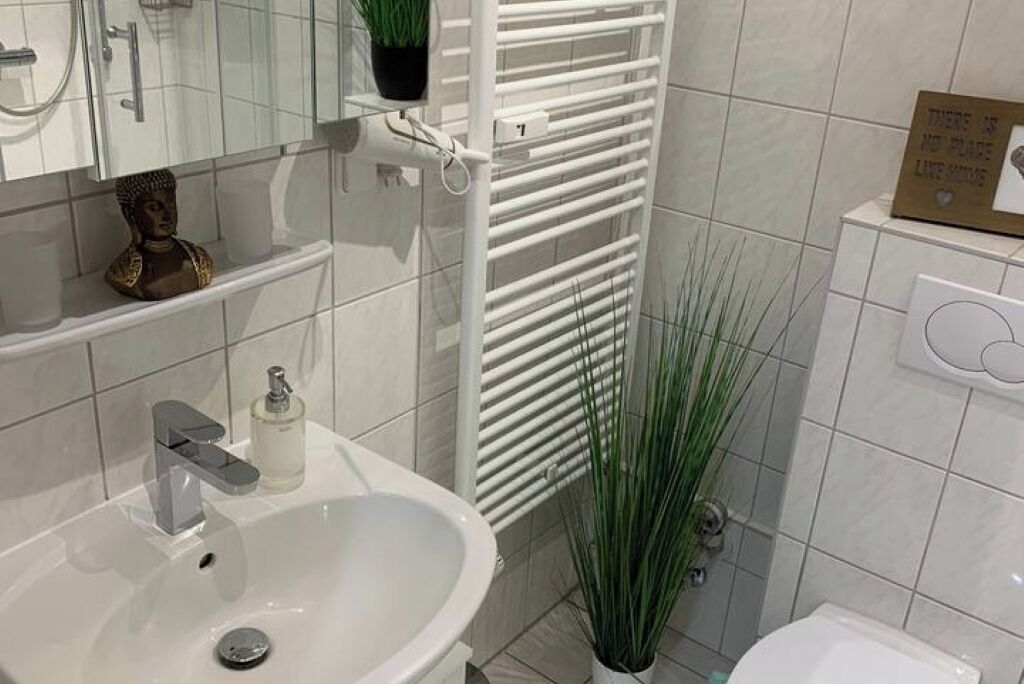 Casa de banho com lavatório branco, porta-toalhas, sanita e uma planta em vaso.