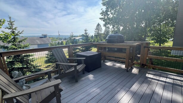 Una terraza de madera con una parrilla, sillas y una mesa.