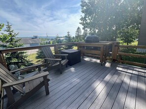 A wooden deck with a grill, chairs, and a table.