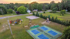 Un campo da tennis circondato da tavoli da picnic e attrezzature per bambini.
