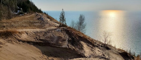 Paesaggio costiero con spiaggia sabbiosa, vegetazione rada e vista aperta sull'oceano.