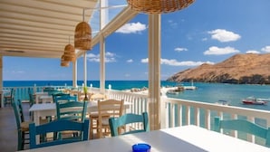 A seaside restaurant with outdoor seating, white tables, and blue chairs, overlooking the sea and boats. - Villa Armi (Pirgos)