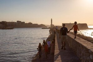 A waterfront promenade with people walking, a lighthouse in the distance, and a clear sky. - Villa Armi (Pirgos)