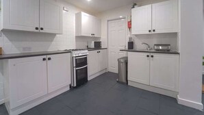 A modern kitchen with white cabinets, a stove, microwave, and a trash bin.