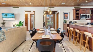 Una cocina moderna con armarios de madera, un comedor con mesa y sillas de madera, y un televisor montado en la pared.
