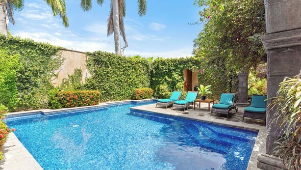 Una piscina con sillones de descanso y vegetación.