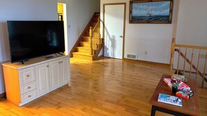 Una sala de estar con un televisor sobre un mueble bajo, una escalera y un cuadro en la pared.