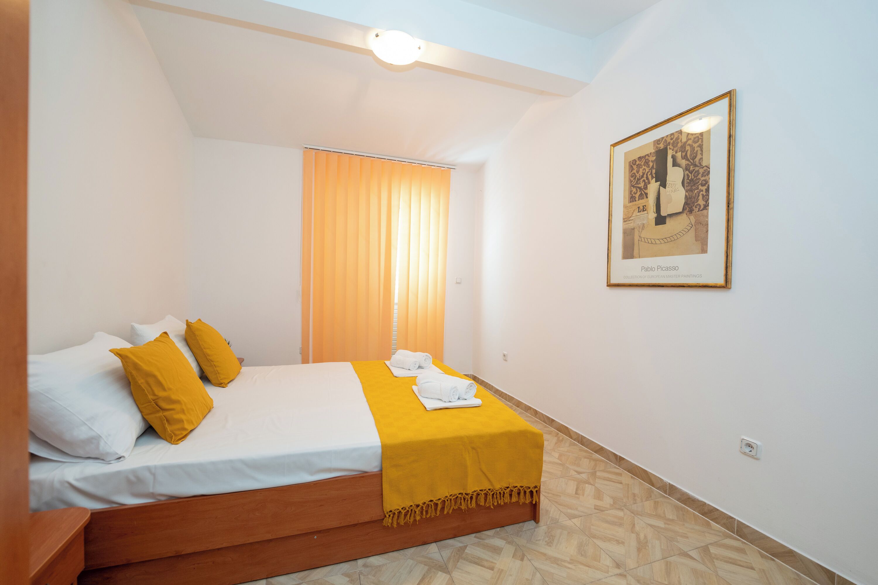 Ein Hotelzimmer mit einem Bett, einer gelben Tagesdecke und einem gerahmten Kunstwerk an der Wand.