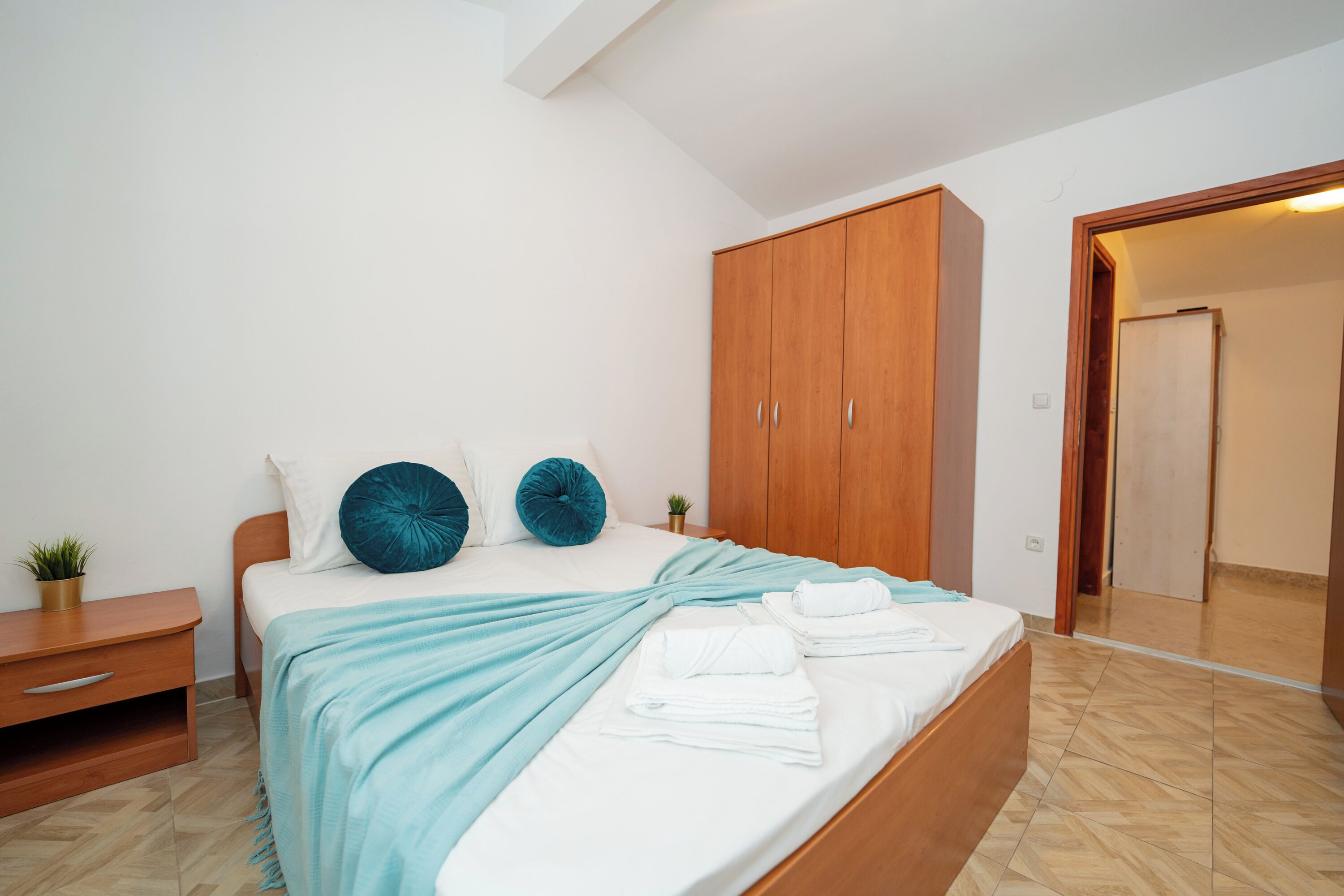 A bedroom with a bed, wooden wardrobe, bedside table, and a small potted plant.