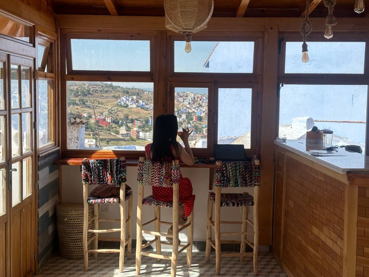 Habitación con vistas a un pueblo a través de amplios ventanales, muebles de madera y una cesta tejida.