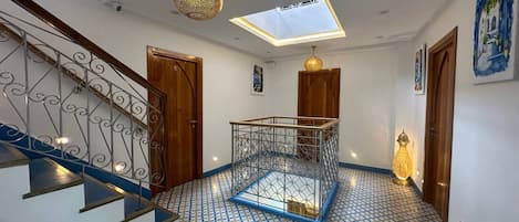 Un pasillo con piso estampado, una escalera con barandal de metal y un tragaluz.
