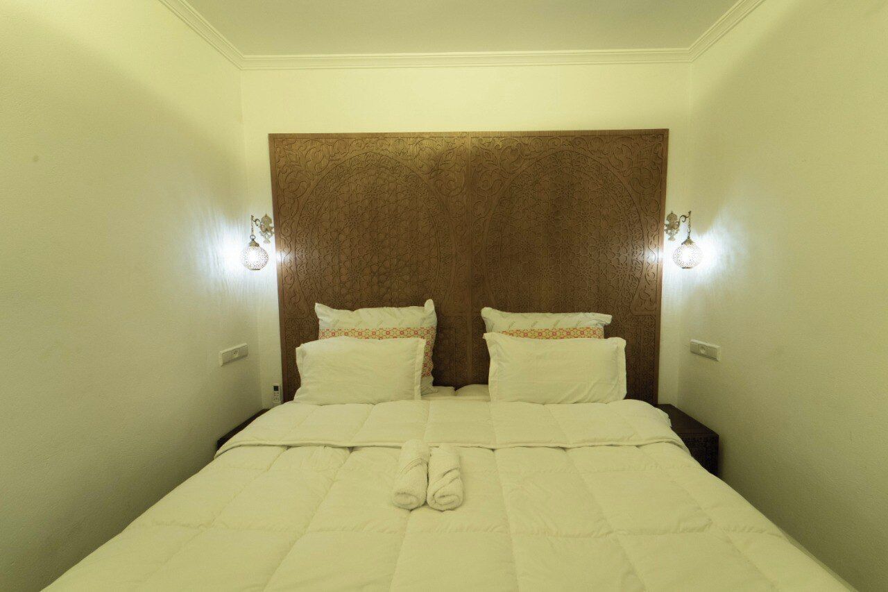 Een hotelkamer met een groot bed, twee bedlampen en een hoofdbord met een decoratief patroon.