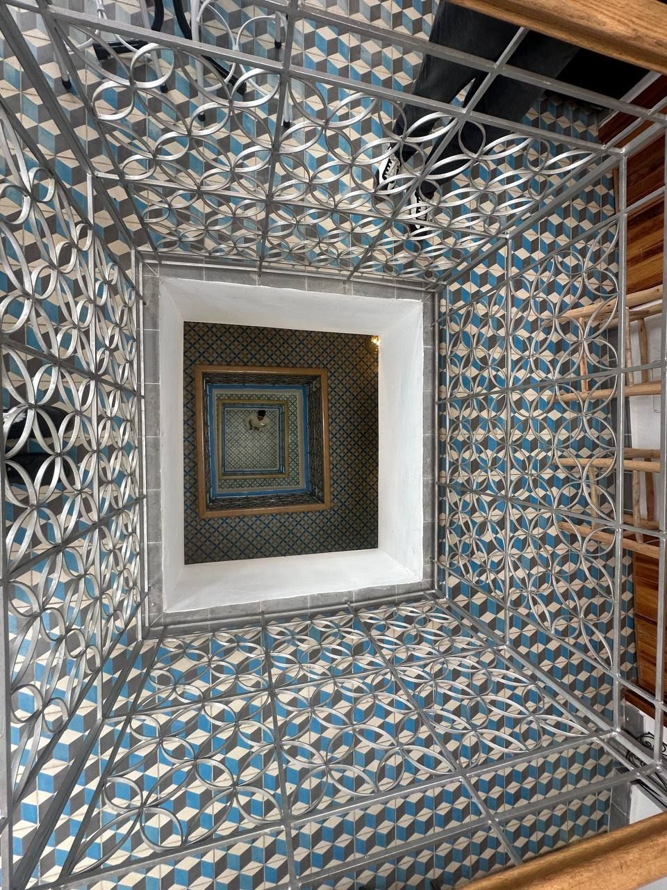 A room with a geometric patterned floor, a central square window, and a metal decorative railing.